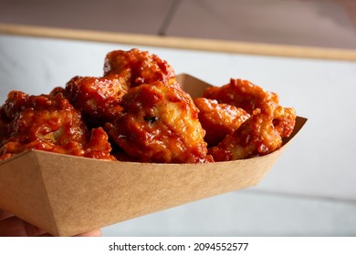 A View Of A Hand Holding A Tray Of Asian Glazed Chicken Wings.