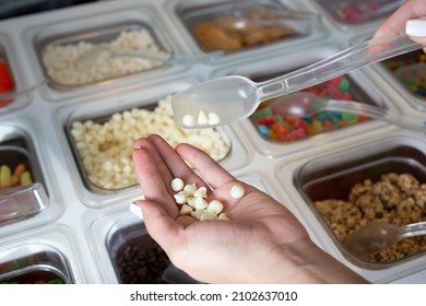 A View Of A Hand Hover Over A Counter Full Of A Variety Of Toppings, Seen At A Local Frozen Yogurt Restaurant.