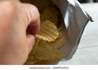 A view of a hand pulling out a wavy potato chip from a product bag. - Powered by Shutterstock