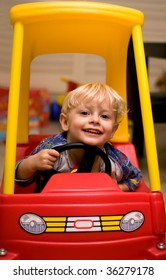 View Of A Happy Small Child In A Red And Yellow Toy Car