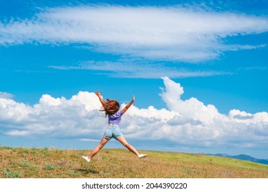 View of a happy young woman jumping on a summer meadow in the air against a blue sky with clouds