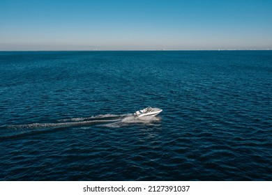 A view from a height of a white speedboat sailing in the birch sea. The motor boat leaves a mark on the water. The concept of water travel and recreation.