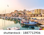 View to Heraklion in the early morning during sun rise, the old port with traditional fishing boats and town with its antient buildings at the background. Selective focus