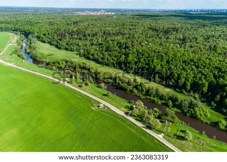 View from a high altitude of a green landscape with a field, river and forest. Water wells located along the river outside the city limits