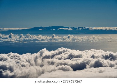 View from high elevation above a dense layer of cumulus clouds looking across the Atlantic Ocean toward the mountainous silhouette of Gran Canaria on the horizon