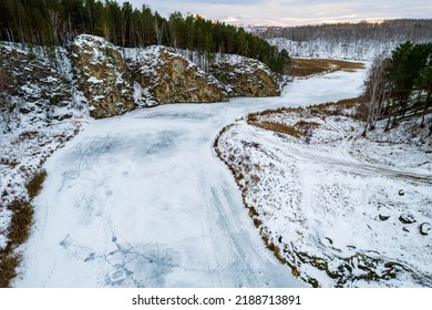 View From A High Point On A Frozen River Covered With Ice, Rocks Along The Banks Of The River. Winter Landscape Aerial View