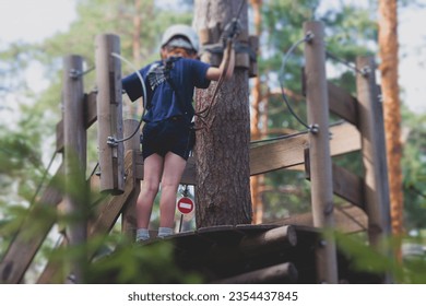 View of high ropes course, kids of climbing in amusement acitivity rope park, passing obstacles and zip line on heights, children teenagers in equipment gear between the trees on heights, summer day - Powered by Shutterstock