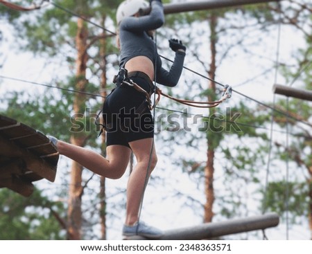 View of high ropes course, process of climbing in amusement acitivity rope park, passing obstacles and zip line on heights in climbing safety equipment gear between the trees om heights, summer day
