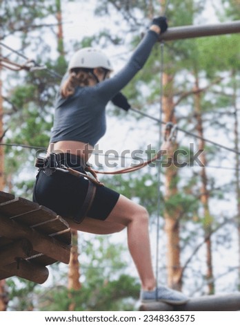 View of high ropes course, process of climbing in amusement acitivity rope park, passing obstacles and zip line on heights in climbing safety equipment gear between the trees om heights, summer day