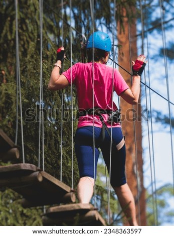 View of high ropes course, process of climbing in amusement acitivity rope park, passing obstacles and zip line on heights in climbing safety equipment gear between the trees om heights, summer day