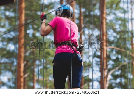 View of high ropes course, process of climbing in amusement acitivity rope park, passing obstacles and zip line on heights in climbing safety equipment gear between the trees om heights, summer day