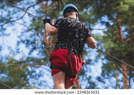 View of high ropes course, process of climbing in amusement acitivity rope park, passing obstacles and zip line on heights in climbing safety equipment gear between the trees om heights, summer day