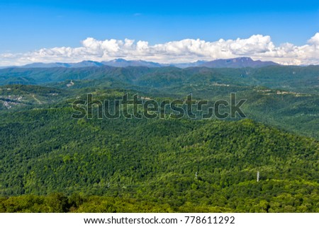 The view of the highland village and Caucasus mountains covered with green forest and snow from the lookout tower on mount Akhun. Khosta district, Adler, Sochi, Russia.