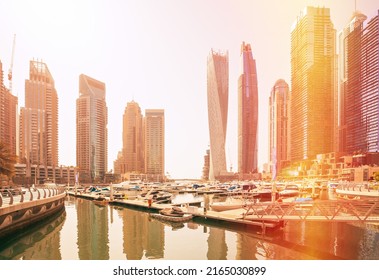 View of high-rise buildings of residential district in Dubai Marina and yachts moored near pier in sunny day. Dubai Marina Towers. Flare sun, film effect, lens flare, glow, film light, flare