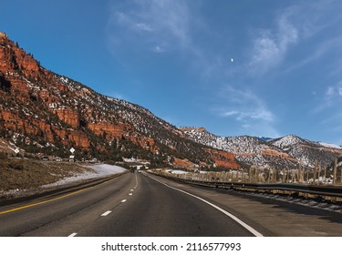 View Of Highway Through Red Rocks Formations In Colorado, USA, In Winter From Moving Car; Moon Rising