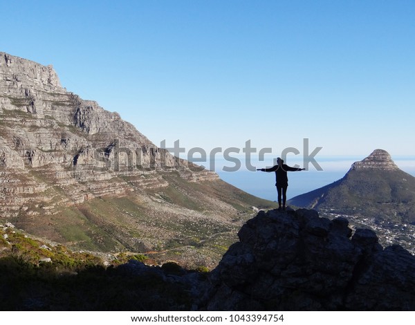 View of a hiker\
in the Table Mountain National Park, Cape Town, South Africa, taken\
from Devil\'s Peak with Lion\'s Head and Table Mountain, and the sea,\
in the background.
