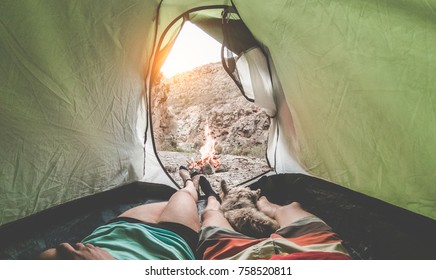 View Of Hikers Couple Inside Tent Camping In Rock Mountains With Their Dog - Sporty People Relaxing After A Trekking Day With Next Fire At Sunset Travel,love,nature And Healthy Concept - Focus On Feet