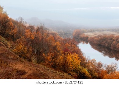 View from the hill to the river with autumn trees along the banks. Foggy morning