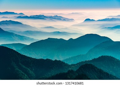 View of Himalayas mountain range with visible silhouettes through the colorful fog from Khalia top trek trail. Khalia top in himalayan region of Kumaon, Uttarakhand, India. - Powered by Shutterstock