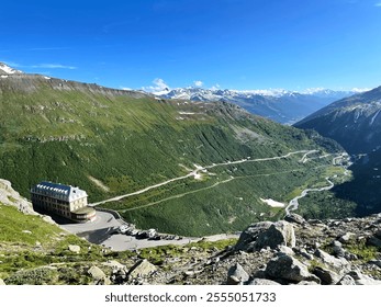 A view of a historic mountain hotel surrounded by lush green hills and a winding alpine road. - Powered by Shutterstock