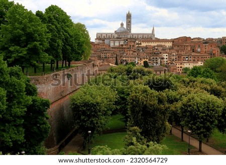 View of the historic part of the city of Siena with the Duomo di Siena in the center of the photo and the walls and park of the Fortezza Medicea in the foreground in the Tuscany region of Italy