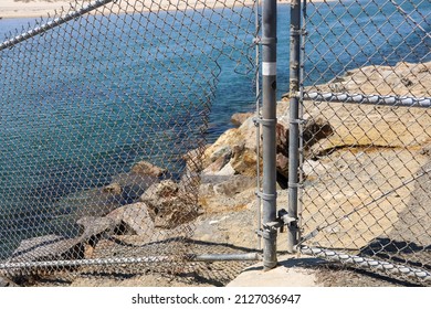 View of a hole on a broken chain link fence. Passage for trespassers.