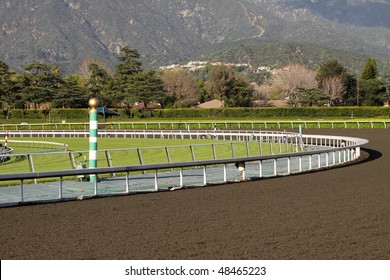 View Of A Horse Racing Track With Mountains In Background. Focus On Green And White Striped Eighth Pole.