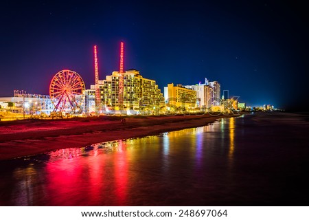 View of hotels and rides along the boardwalk at night from the fishing pier in Daytona Beach, Florida.