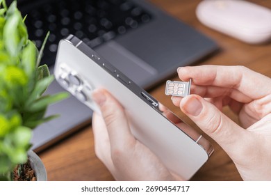 View of human hands inserting a dual nano SIM card into a sleek white mobile smartphone, demonstrating essential telecommunication setup and global data access