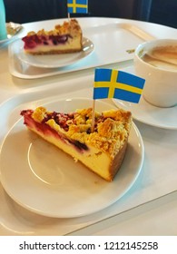 View Of Ikea Berry Cheesecakes With Swedish Flags On An White Plate And Coffee Or Cappuccino. Ikea Shopping Or Food Concept