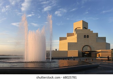 A view of the imposing Museum of Islamic Art in Doha, Qatar, Arabia under a cloudy winter sky, with the water catching the evening sun.