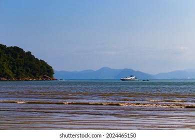 View Of Indaia Beach With Its Calm Sea, In The Background Motorboat Heading To The Backwater Near The Rocks And Distant Mountain Range Covered By A Fine Mist.