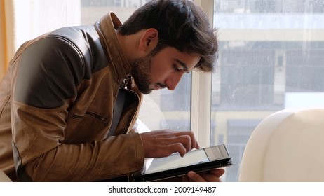A view of an Indian guy in a leather jacket sitting down and looking at his tablet at home