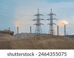 A view of an industrial area featuring power lines, smoke stacks, and emissions. The image highlights the impact of industrial production on the environment, focusing on pollution and infrastructure.