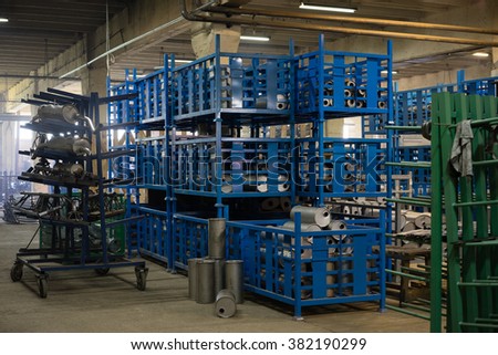 view of an industrial hall, with big blue, green, and grey metallic bins, containing different elements which make up exhaust pipes and accessories