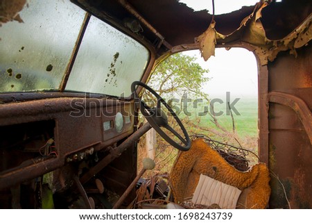 View from the inside of an abandoned rusty truck on a rural property with fog in the background.
