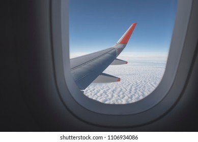 View From Inside Airplane Window. Looking Outside At The Airplane Wing Seeing Clouds And A Blue Sky.