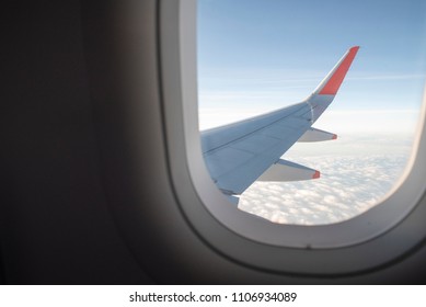 View From Inside Airplane Window. Looking Outside At The Airplane Wing Seeing Clouds And A Blue Sky.