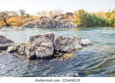 A View From Inside The Boat Looking At The West Bank Of The Nile River Showing Nature And Desert And Granite Rocks Along With The Flow Of Water Coming From Africa 