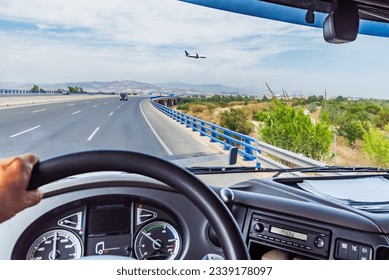 View from inside the cabin of a truck driving on a highway and a plane flying at low altitude