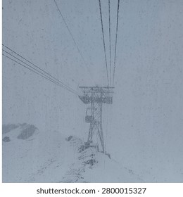 A view from inside a cable car looking out at a towering support structure for the lift system, set against a backdrop of snowy mountain peaks partially obscured by dense fog and precipitation.