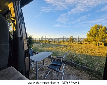 View from Inside Camper Van with Open Door at Sunset – Table and Chairs in Golden Field.
