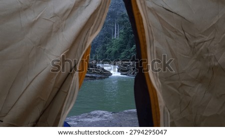 View from inside a camping tent overlooking a scenic tropical river waterfall during an outdoor wilderness adventure trek