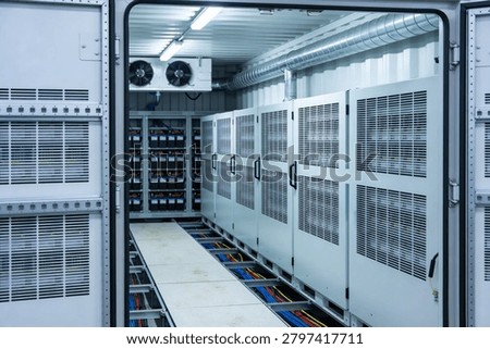 A view inside a climate-controlled containerized data center featuring rows of server cabinets and a battery backup system with visible cabling