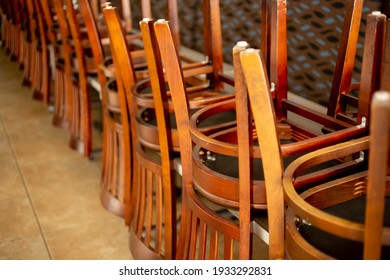 A View Inside A Closed Restaurant Dining Room, Featuring A Line Of Chairs Turned Over On The Tables. 