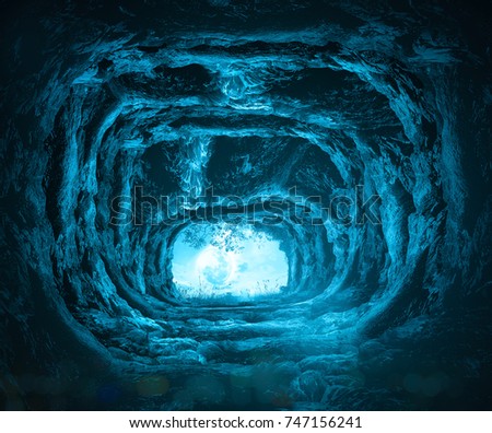 View from inside a dark stone cave looking out towards a bright blue light at the exit, concept of hope, freedom, discovery, and finding the way out from darkness.