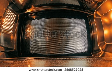 View from inside an empty microwave oven as a hungry man looks in from the kitchen. Warm light and metal reflections create a dramatic, futuristic atmosphere.
