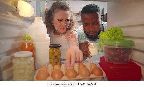 View From Inside Fridge Of Young Multiracial Couple Feeling Bad Smell. Diverse Man And Woman Looking For Source Cause Of Awful Smell Of Rotten Food In Refrigerator