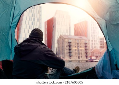 View from inside of a homeless tent. Man in dark dirty cloths sitting by the entrance looking at rich high value district houses. Living during financial crisis concept. Dreaming on better future.