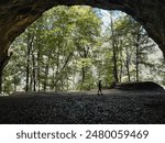 View from inside a large cave looking out to the forest. A single man in silhouette strolls casually. Located within Starved Rock State Park in LaSalle County, Illinois, USA.